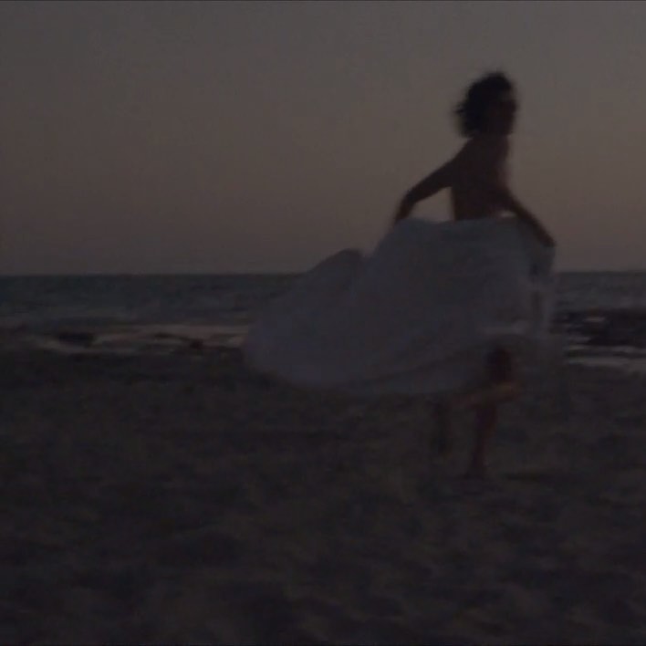 Figure running across a sandy beach at dusk wearing a large flowing white garment by photographer Camilla Armbrust