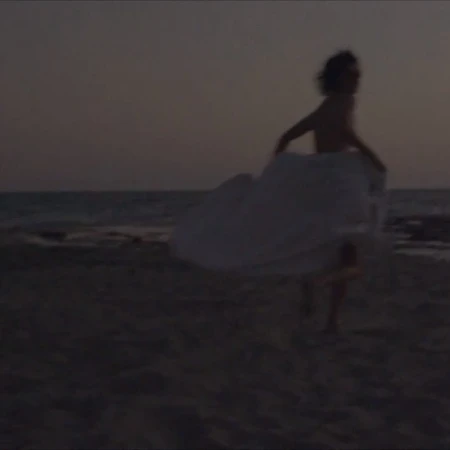 Figure running across a sandy beach at dusk wearing a large flowing white garment by photographer Camilla Armbrust