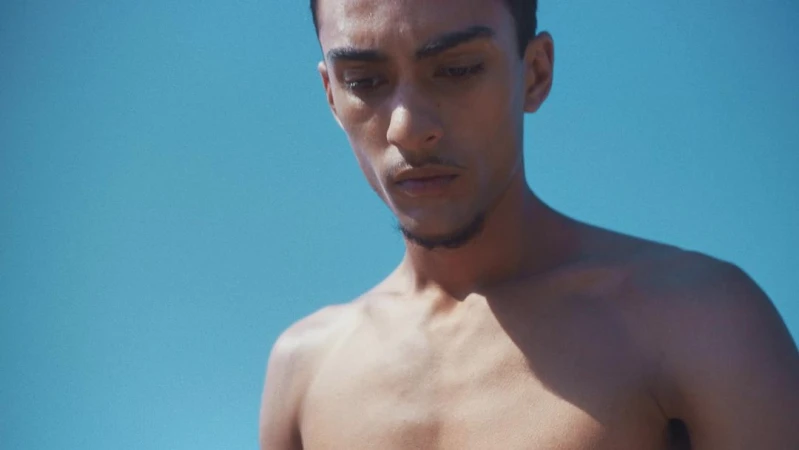 Portrait of a shirtless young man looking down against a bright blue sky background captured by photographer Camilla Armbrust.