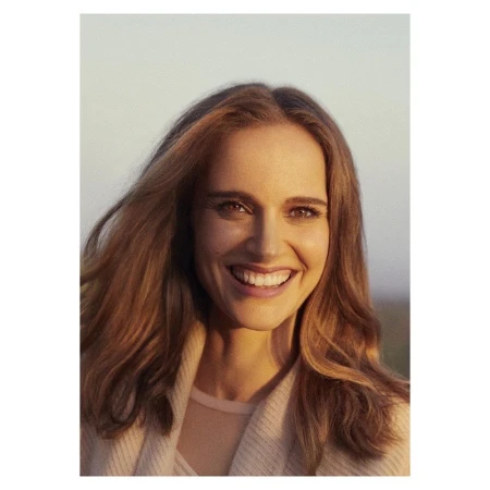 Portrait of Natalie Portman smiling in golden hour sunlight wearing a light knitted sweater against a soft outdoor background.