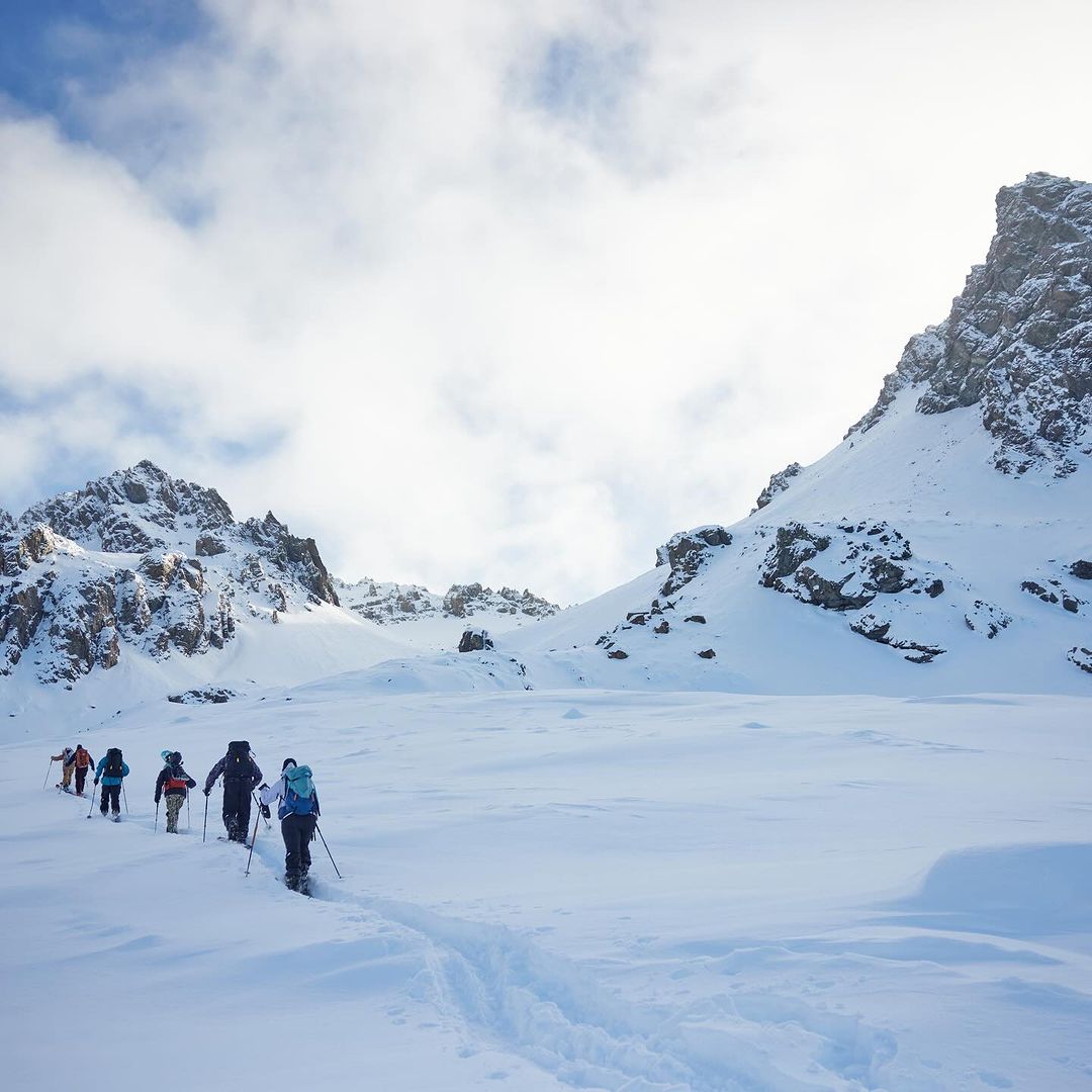 A group of six people is ski touring in a snowy mountain landscape under a cloudy sky, showcasing winter sports and outdoor adventures.