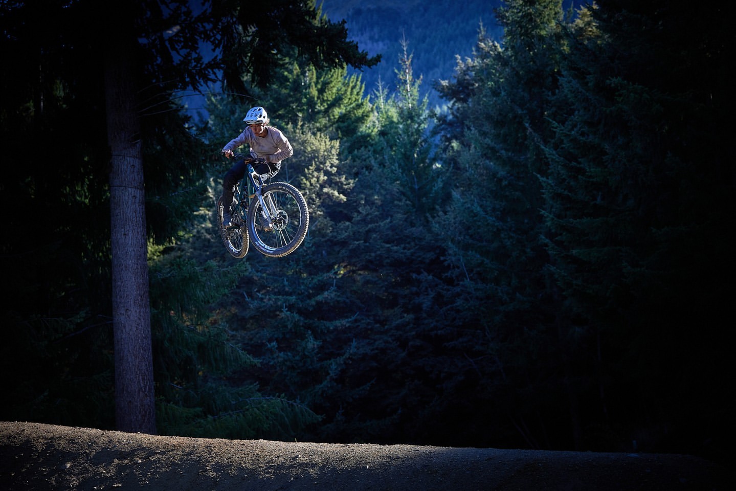 An adult rides a mountain bike, soaring through the air in a forest setting, demonstrating extreme sports and outdoor activities.