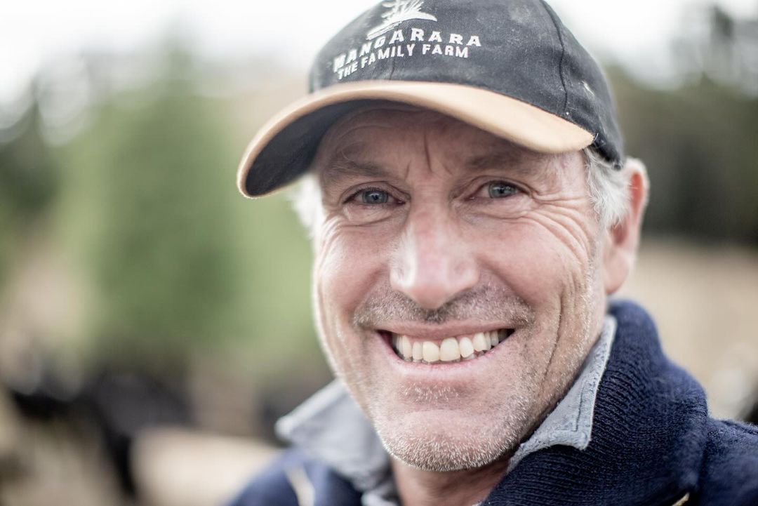 Close-up portrait of a smiling middle-aged man wearing a 'Wangarara The Family Farm' cap, set against a blurred outdoor backdrop.