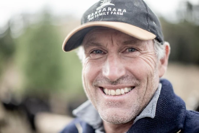 Close-up portrait of a smiling middle-aged man wearing a 'Wangarara The Family Farm' cap, set against a blurred outdoor backdrop.