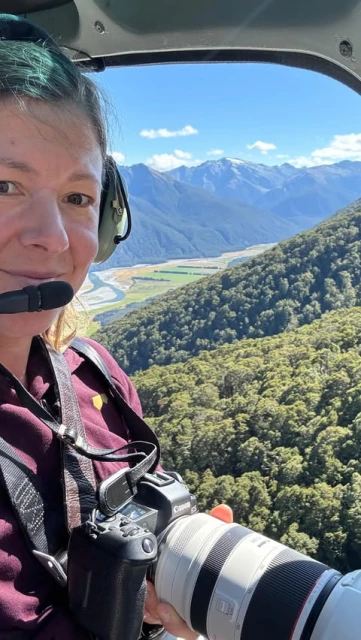 Adult female photographer with camera in helicopter, scenic mountain landscape view.