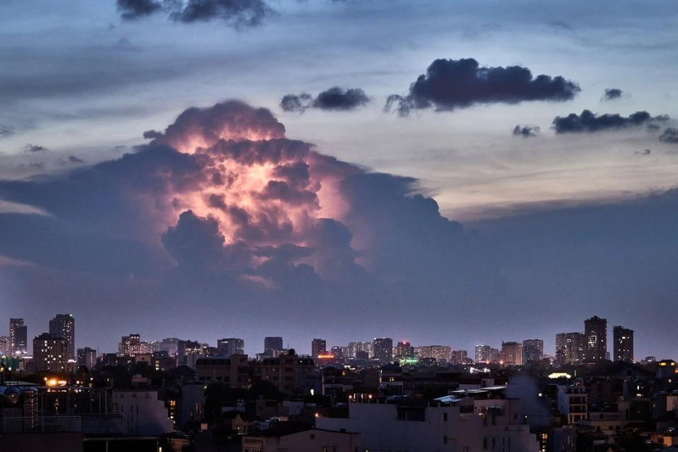 Night city skyline view under a dramatic, cloudy sky. Cityscape at twilight with illuminated buildings and a cloudy, pink-lit sky.