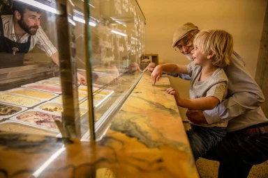 An elderly man and a young boy looking at ice cream in a display case, photographed by Camilla Rutherford