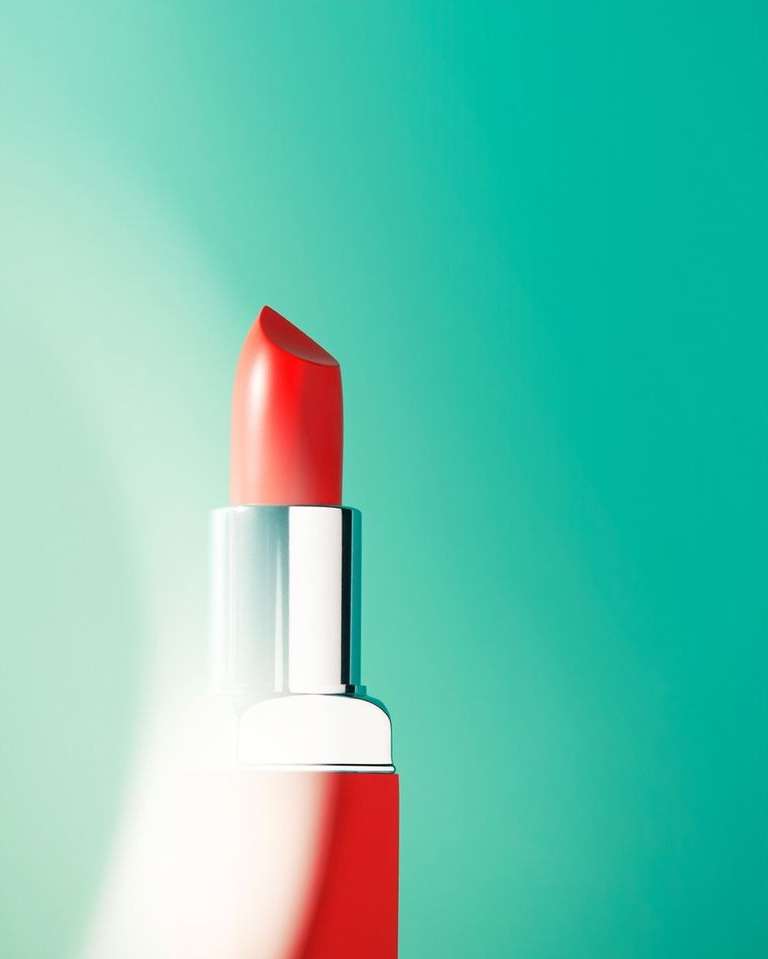 Close-up studio shot of red lipstick with silver tube against teal and light teal gradient background, beauty and cosmetics
