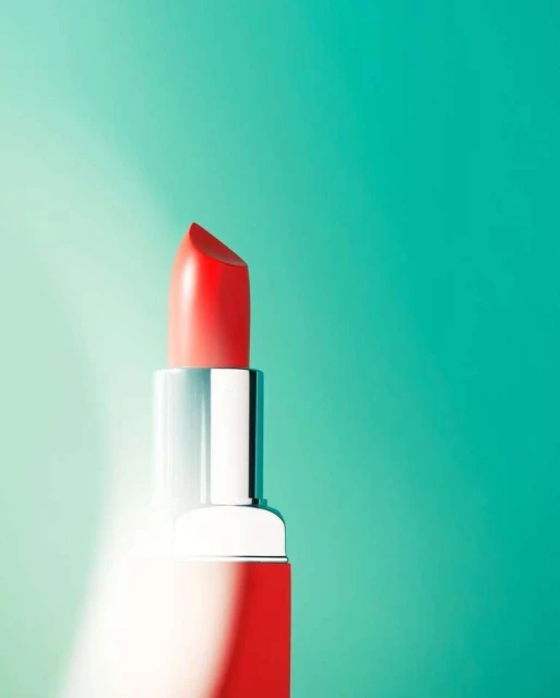 Close-up studio shot of red lipstick with silver tube against teal and light teal gradient background, beauty and cosmetics