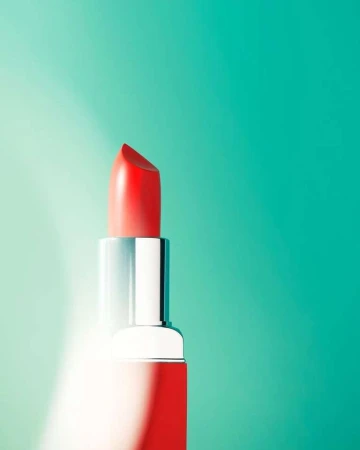 Close-up studio shot of red lipstick with silver tube against teal and light teal gradient background, beauty and cosmetics
