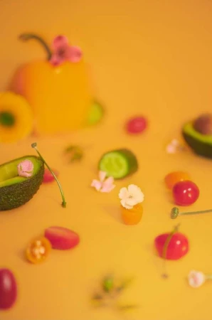 Artful food still life: yellow bell pepper, halved avocado, sliced cucumber, kumquats, cherry tomatoes, and delicate white flowers.