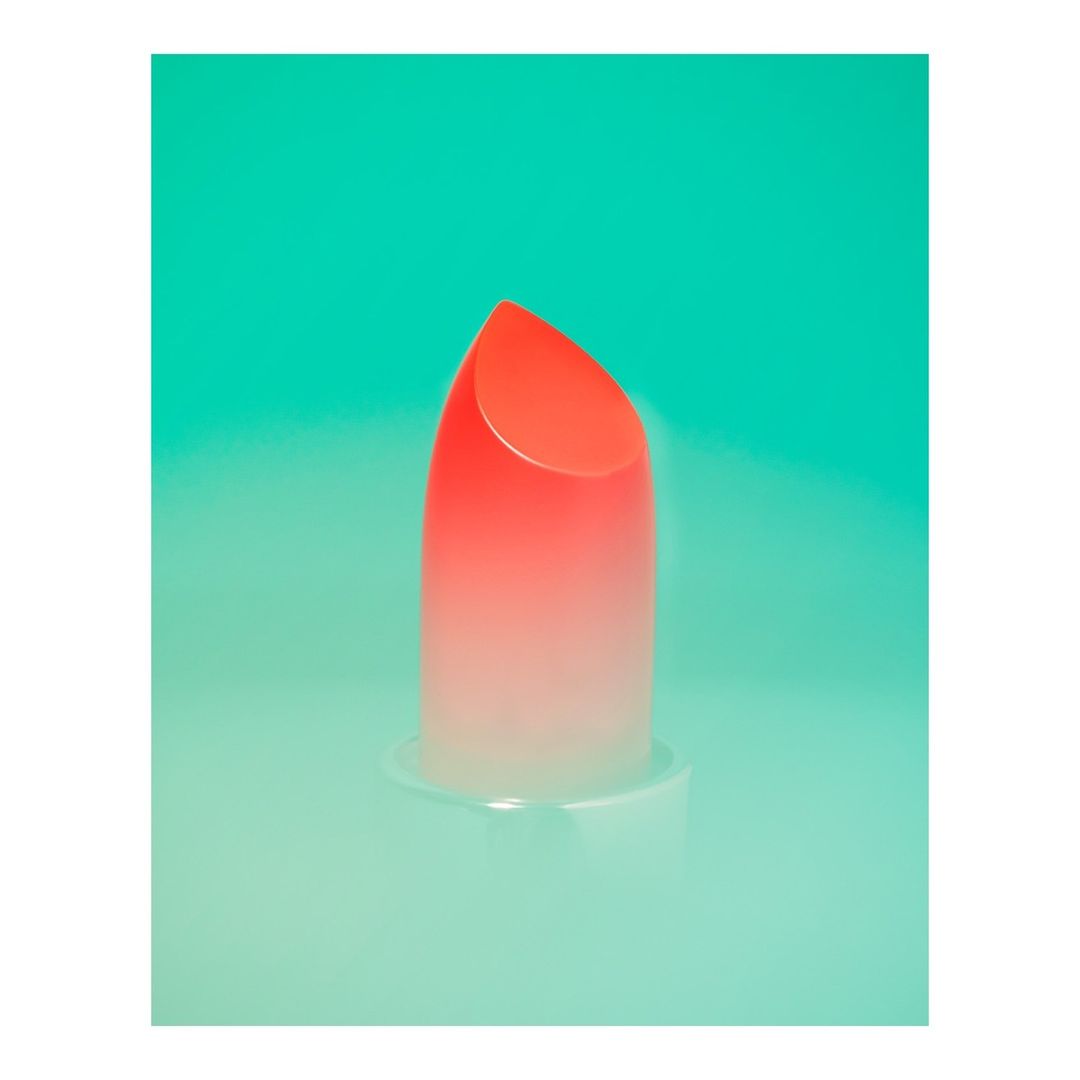 Close-up shot of a vibrant orange lipstick, its color smoothly transitioning to white, against a bright cyan background, emphasizing beauty.