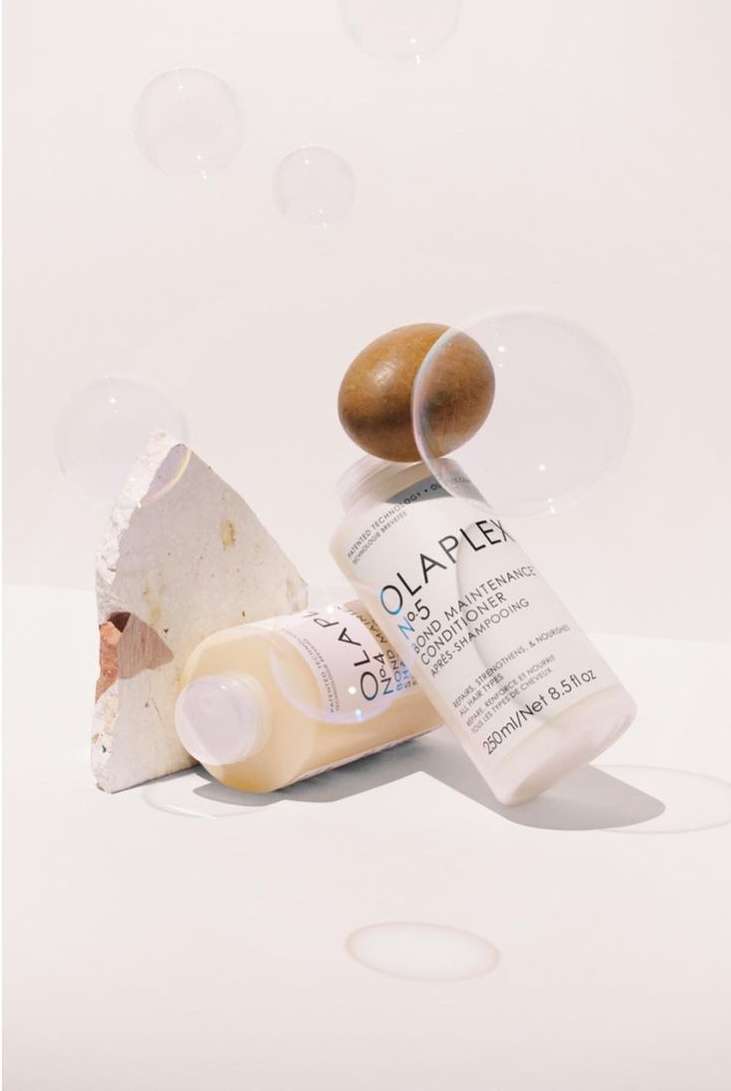 Close-up studio shot of two Olaplex No. 5 Bond Maintenance Conditioner bottles with neutral stone and an egg. Hair care concept.