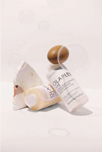 Close-up studio shot of two Olaplex No. 5 Bond Maintenance Conditioner bottles with neutral stone and an egg. Hair care concept.