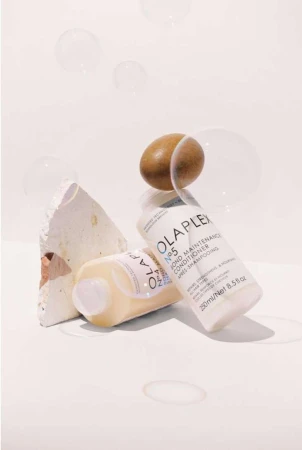 Close-up studio shot of two Olaplex No. 5 Bond Maintenance Conditioner bottles with neutral stone and an egg. Hair care concept.