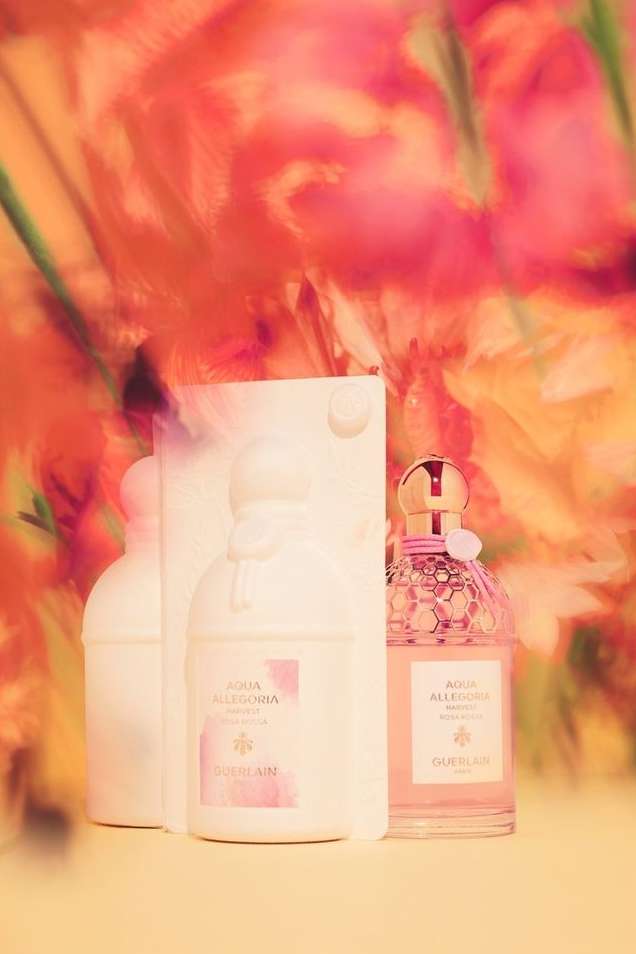Still life of three pink and white Guerlain Aqua Allegoria perfume bottles against a blurred pink, orange, and white floral background.