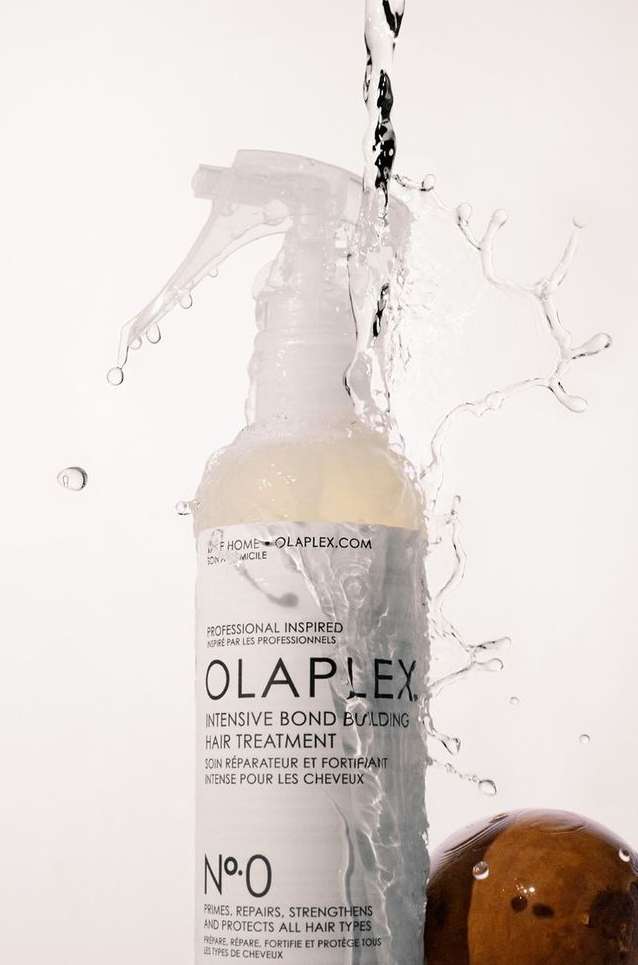 Olaplex No. 0 hair treatment bottle with water splashing around it, against a white background. Beauty and haircare product photography.