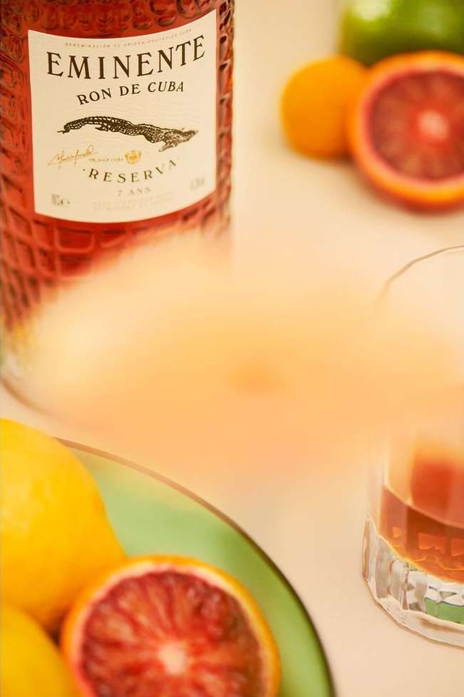 Eminente Ron de Cuba bottle with assorted citrus fruits on a light surface, capturing a vibrant and refreshing beverage scene.
