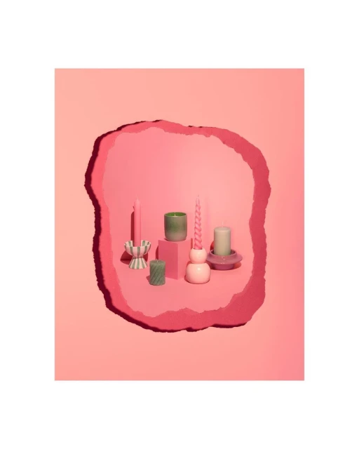 Assortment of decorative candles in various shapes and colors arranged on pink platforms against a layered pink background.