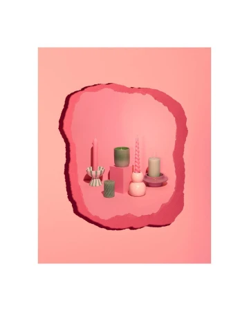 Assortment of decorative candles in various shapes and colors arranged on pink platforms against a layered pink background.