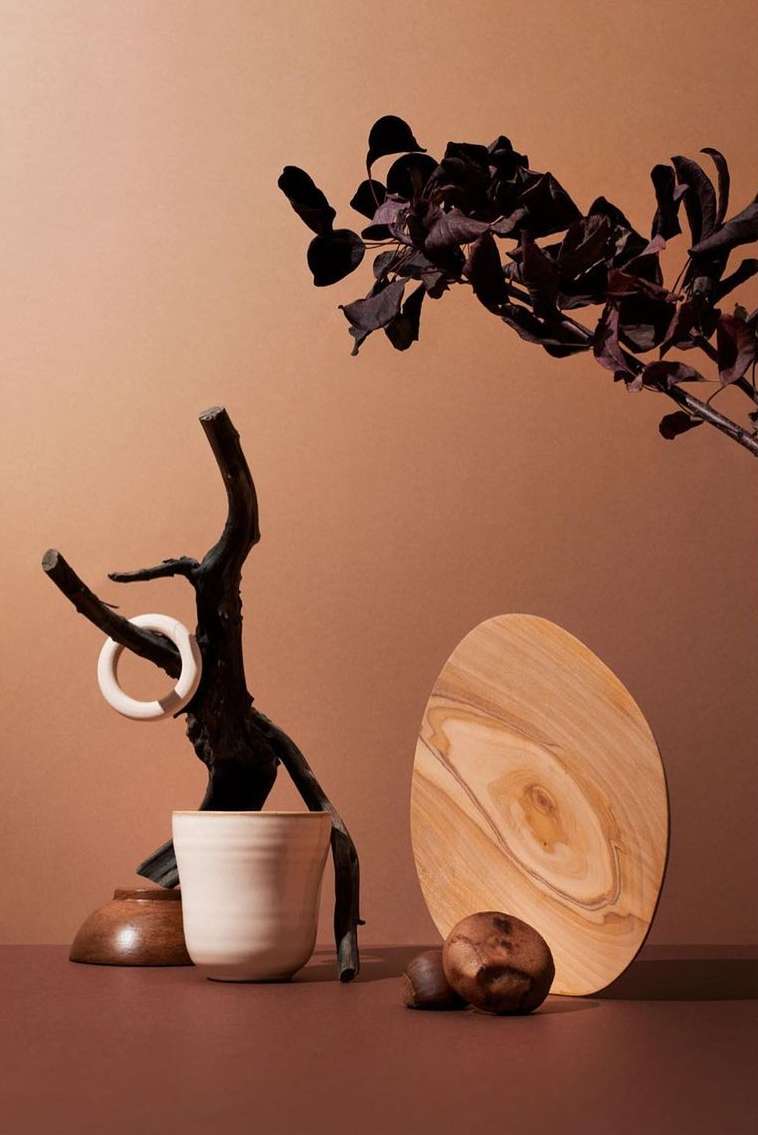 Still life of a wooden cutting board, ceramic cup, and decorative tree branch on a brown surface against a brown background.