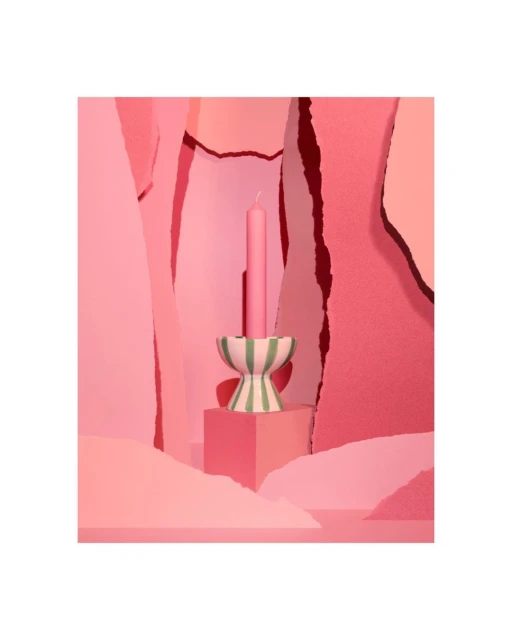 Pink candle in a striped candle holder sits on a cube against a geometric background in various shades of pink for a playful, modern look.