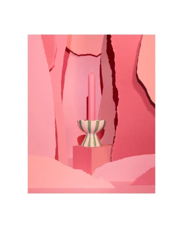 Pink candle in a striped candle holder sits on a cube against a geometric background in various shades of pink for a playful, modern look.