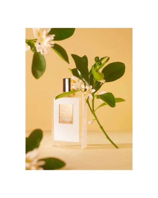Still life shot of a perfume bottle featuring white flowers and green leaves, set against a soft yellow backdrop, product photography.