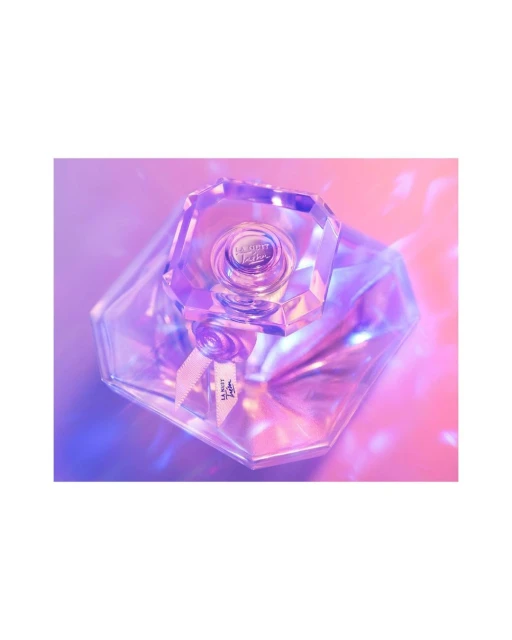 Close-up product shot of a crystal perfume bottle on a pink and purple gradient background with geometric light patterns. Beauty product.
