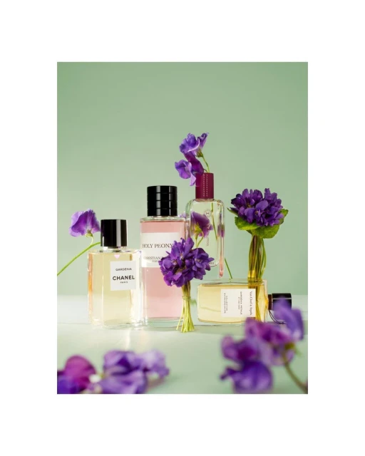 Four perfume bottles displayed with purple flowers against a light green backdrop, creating a beauty and fragrance themed studio still life.