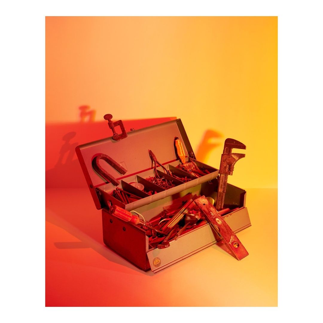 Metal toolbox filled with various hand tools including a wrench, level, and pliers, illuminated by orange and red light in a studio.