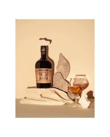 A still-life photograph featuring a bottle of Diplomático rum, a tasting glass with amber liquid, and decorative stone pieces against a neutral backdrop.