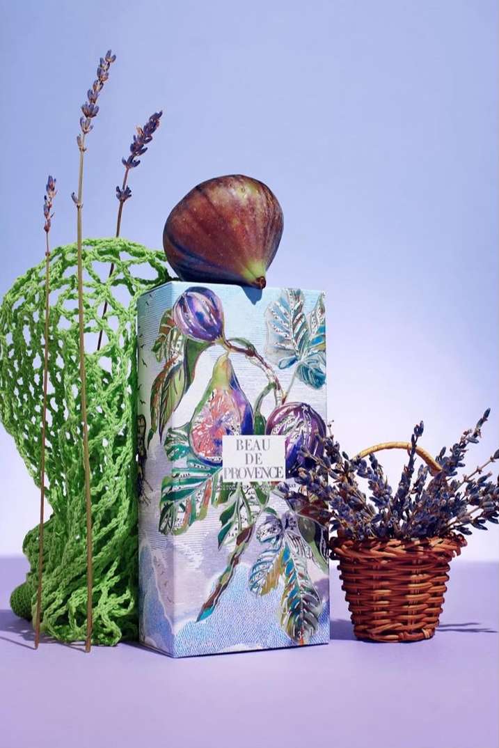 Artistic still life composition featuring a fig fruit atop a Beau de Provence box, complemented by lavender and a green mesh bag.