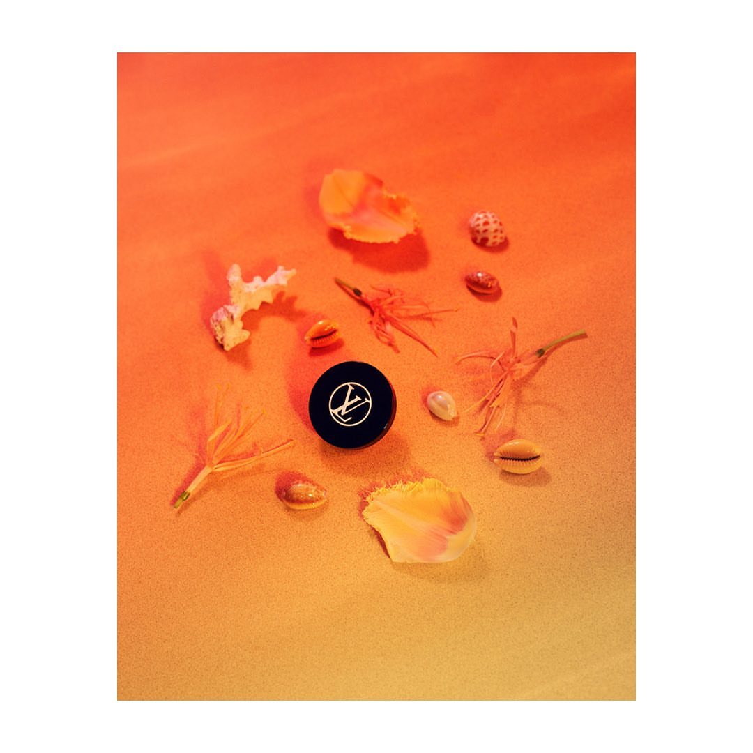 Still life shot of black cosmetic container surrounded by seashells and flower petals on an orange background, product photography.