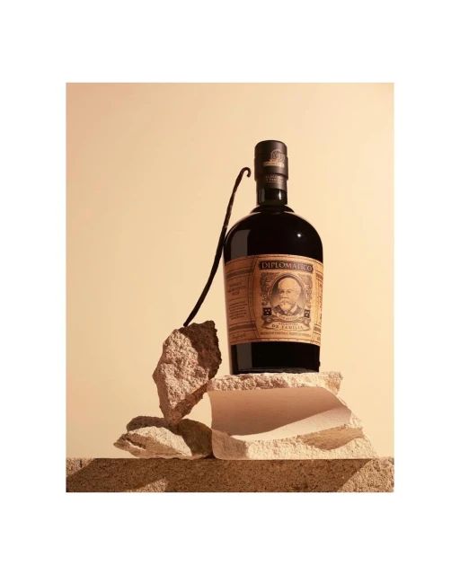 Rum bottle sits atop stacked stones with a vanilla bean, set against a soft tan backdrop. Perfect for food and beverage marketing.
