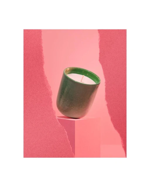 Elevated green ceramic candle holder with white candle on pink cube and pink textured backdrop. Stylish interior accent.