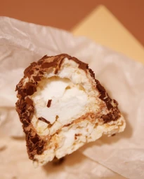 Close-up of a halved chocolate-coated meringue pastry on white crumpled parchment paper
