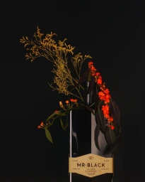 Black coffee liqueur bottle decorated with dried golden foliage and bright orange flowers against a dark background