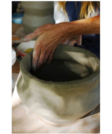 Close-up shot of a person's hands shaping a gray clay pot, showcasing the pottery process and craftsmanship in a studio setting.