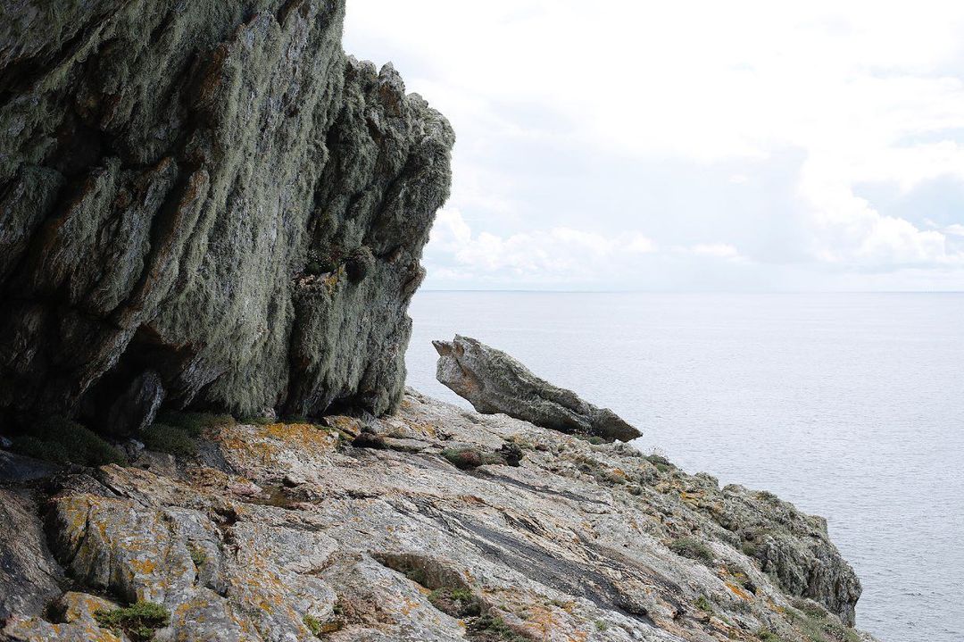 Coastal rock formation with textured gray stone and lichen, meeting the sea and cloudy sky on the horizon, capturing natural beauty.