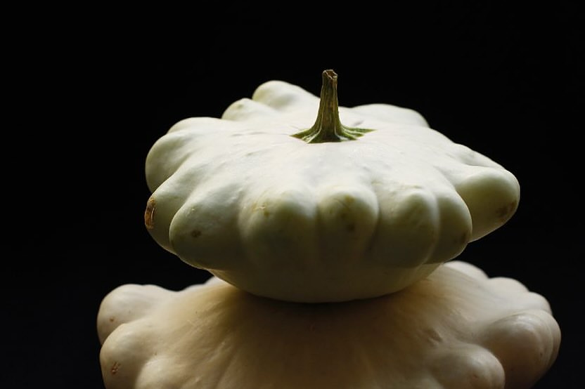 Two stacked patty pan squashes in front of a dark background, showcasing their unique shape and pale green color.