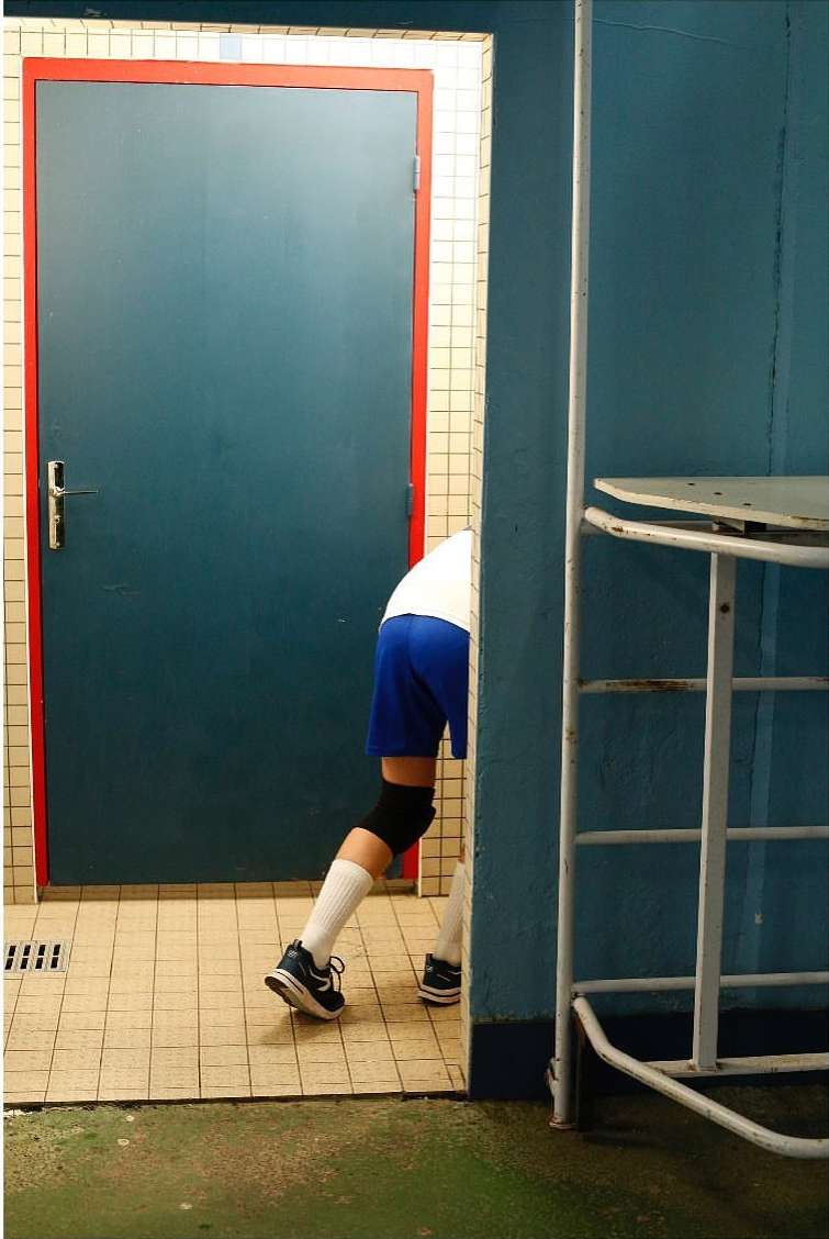 Person emerging from a blue door in a tiled room, wearing blue shorts, white socks, and black sneakers, with a metallic table nearby.