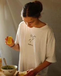 Young woman in white t-shirt squeezing a lemon half into a floral patterned bowl in Paris by photographer Camille Malissen.