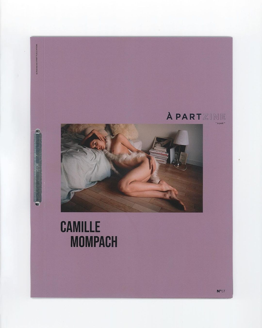 Art magazine cover featuring a reclining person on a bed with a lamp and books in the background, set against a lavender-colored background.