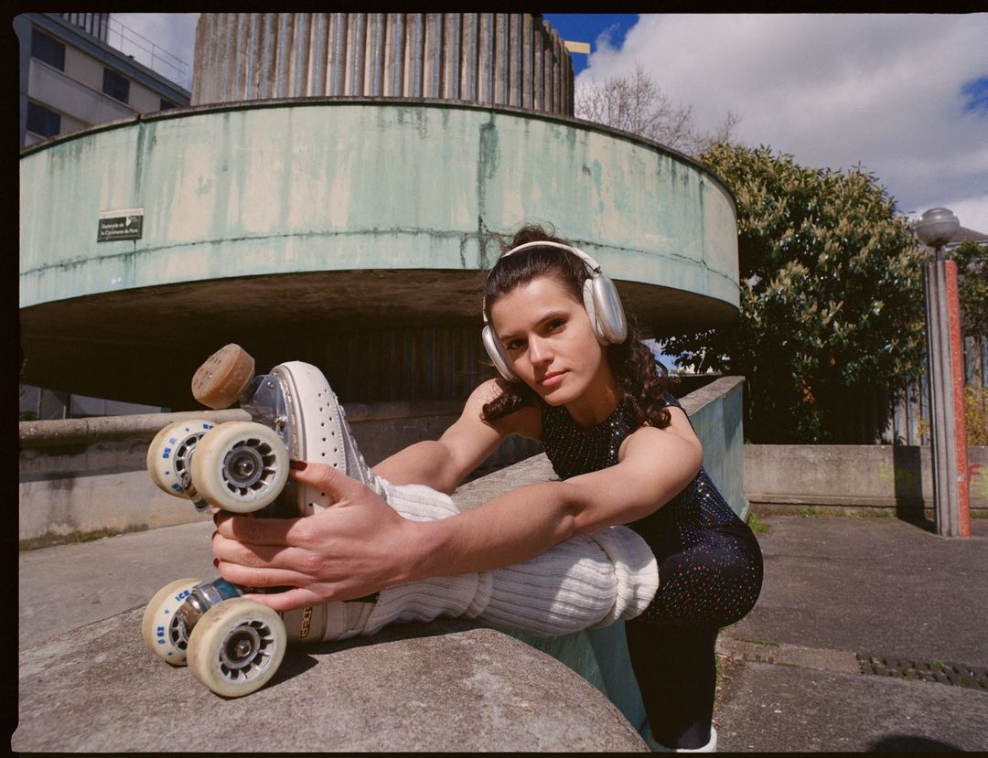 Young woman wearing headphones and roller skates holding her skate wheel outdoors in Paris