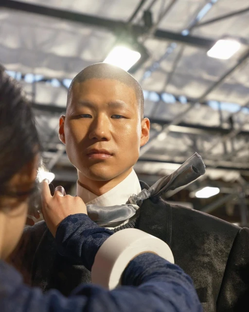 Asian male model having a garment adjusted by a stylist with natural lighting in an indoor setting. Fashion and style concept.