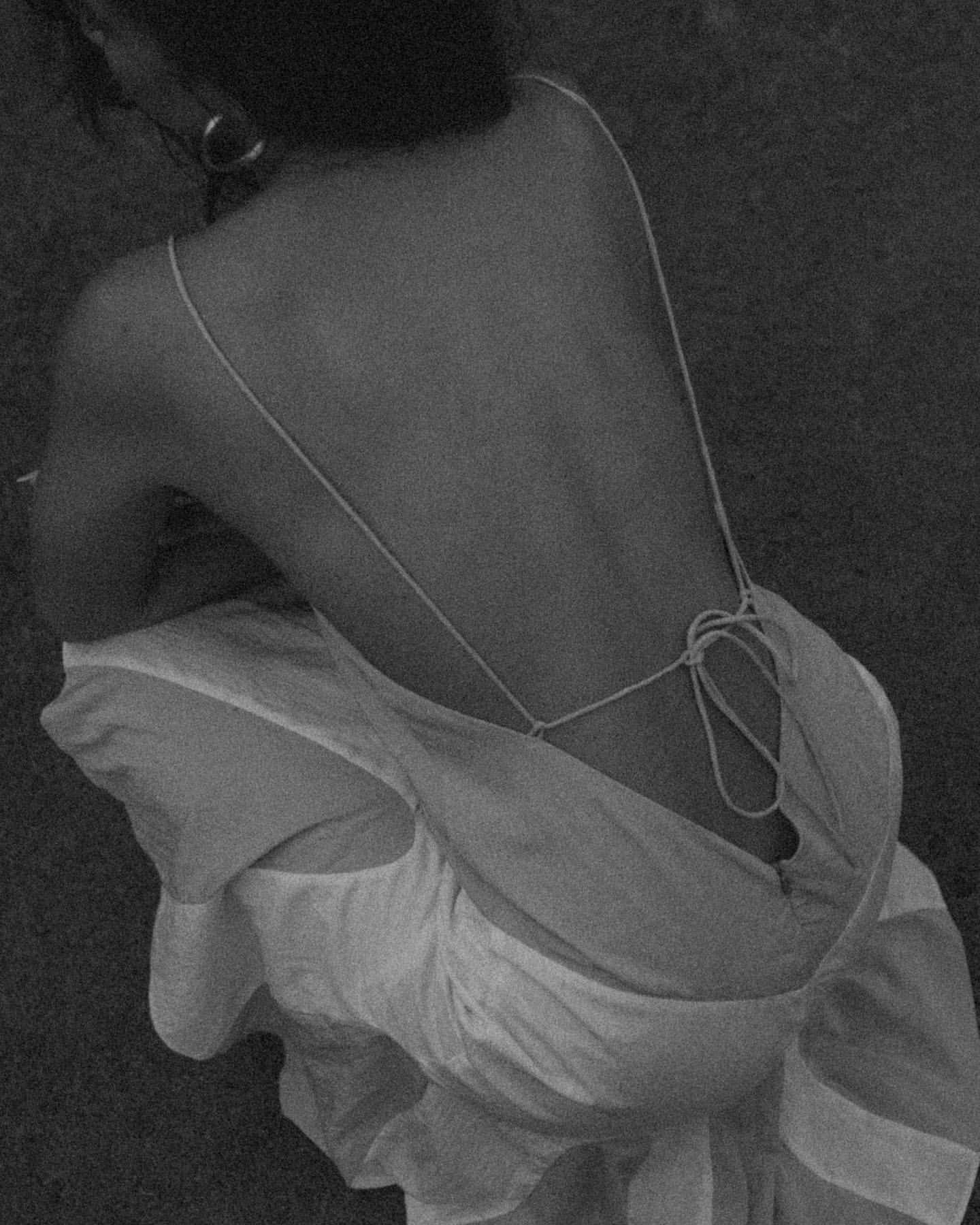 Back view of an adult woman in a dress kneeling with silver hoop earrings in a black and white outdoor image.