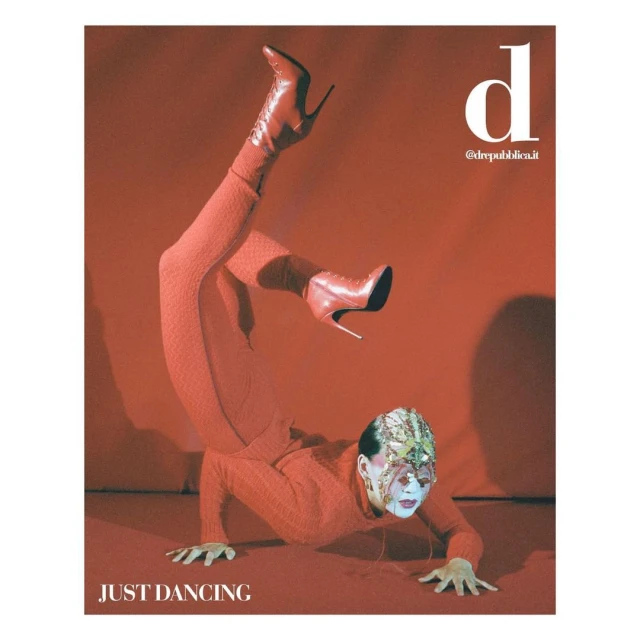 A person in red clothing and high-heeled boots performing a handstand on a red background, appearing on a magazine cover with white text.