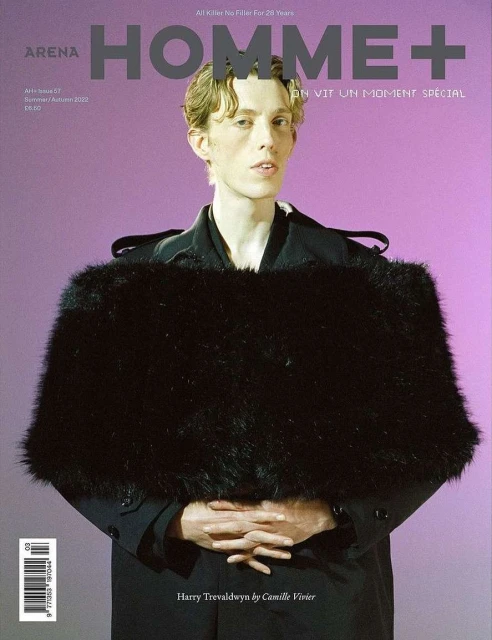 Arena Homme+ magazine cover features a male model in a black coat with faux fur stole against a lilac backdrop, showcasing fashion editorial.