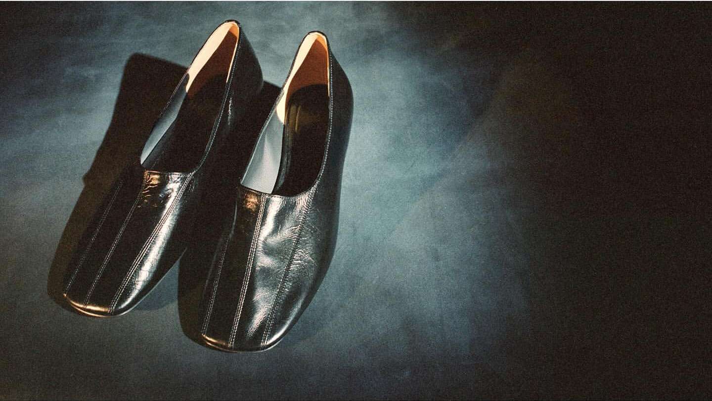 Pair of black leather flats showcased on a dark textured surface with soft lighting, creating a modern and stylish visual.